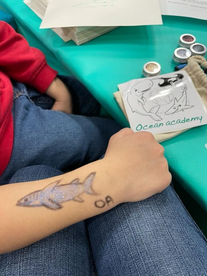 Bras d'un enfant avec un coloriage de requin au stand Ocean academy du salon de la plongée.