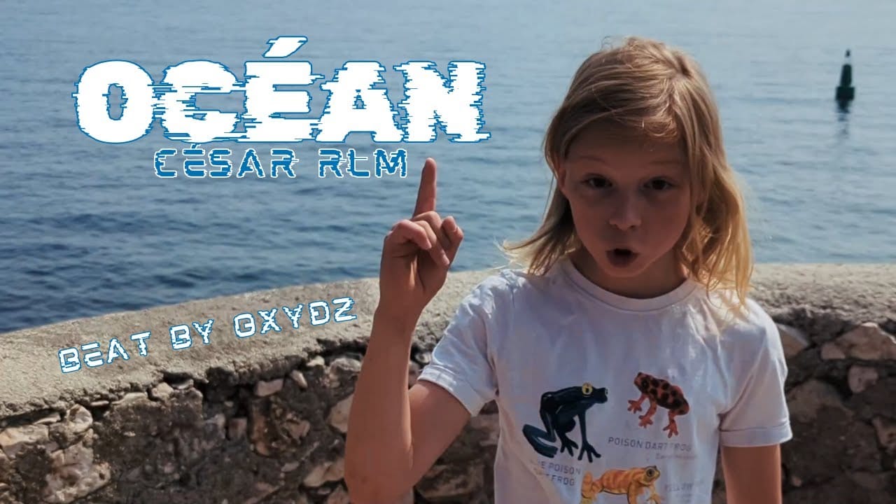 César debout en bord de mer, avec le doigt levé vers le titre de sa chanson : océan