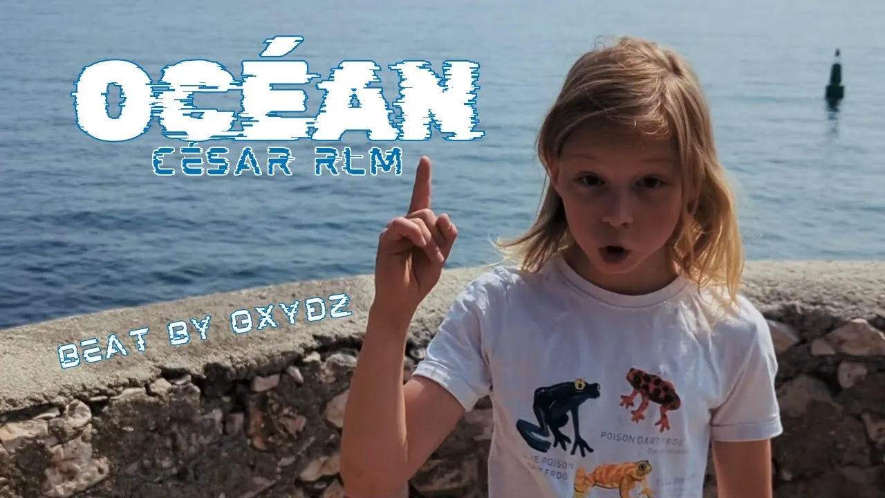 César debout en bord de mer, avec le doigt levé vers le titre de sa chanson : océan