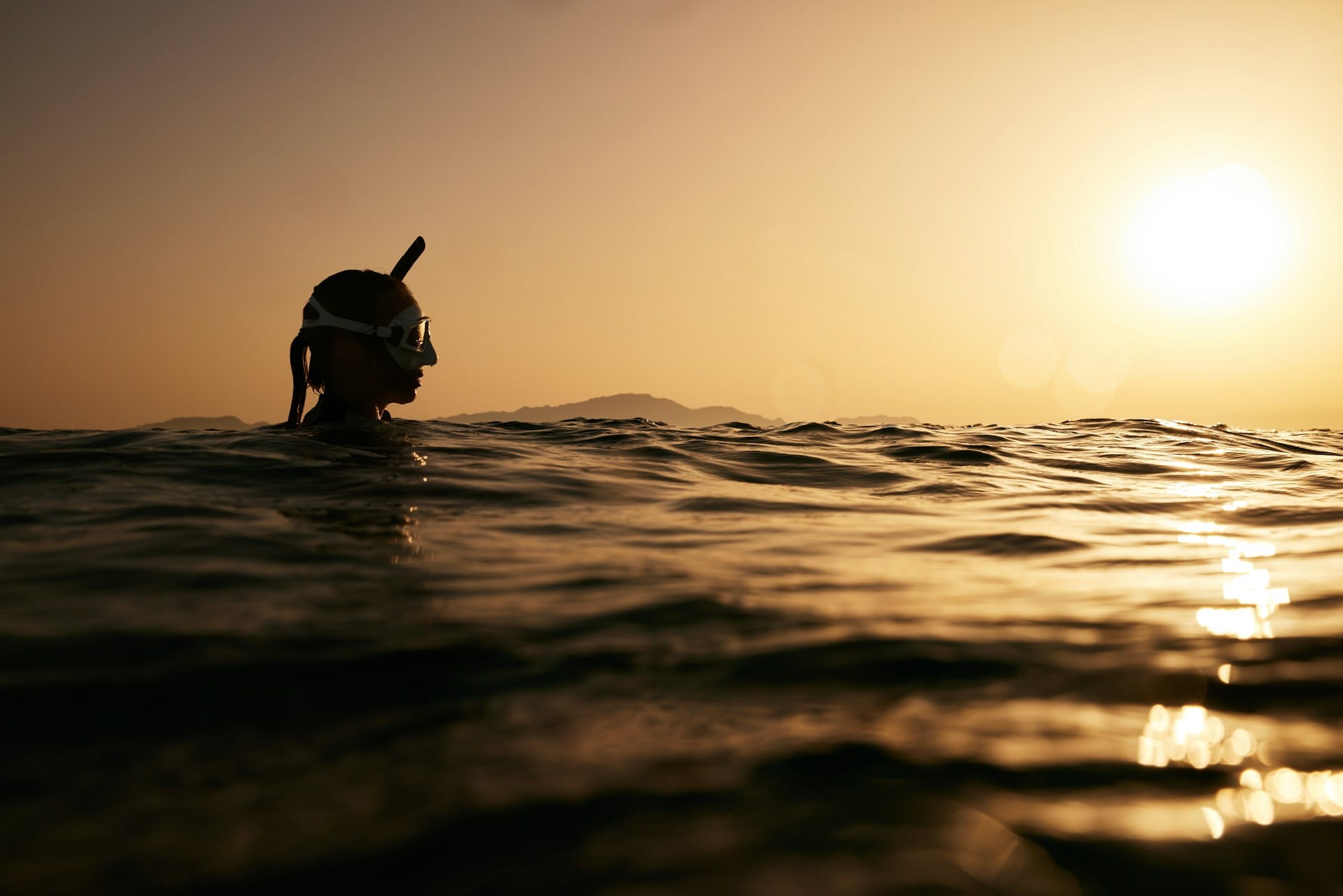 une plongeuse avec son masque et tube en surface au coucher du soleil
